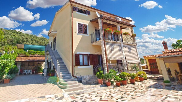 A two-story building with a staircase leading to the entrance, potted plants, and a clear blue sky with clouds. - Apartment 539 (Medulin)