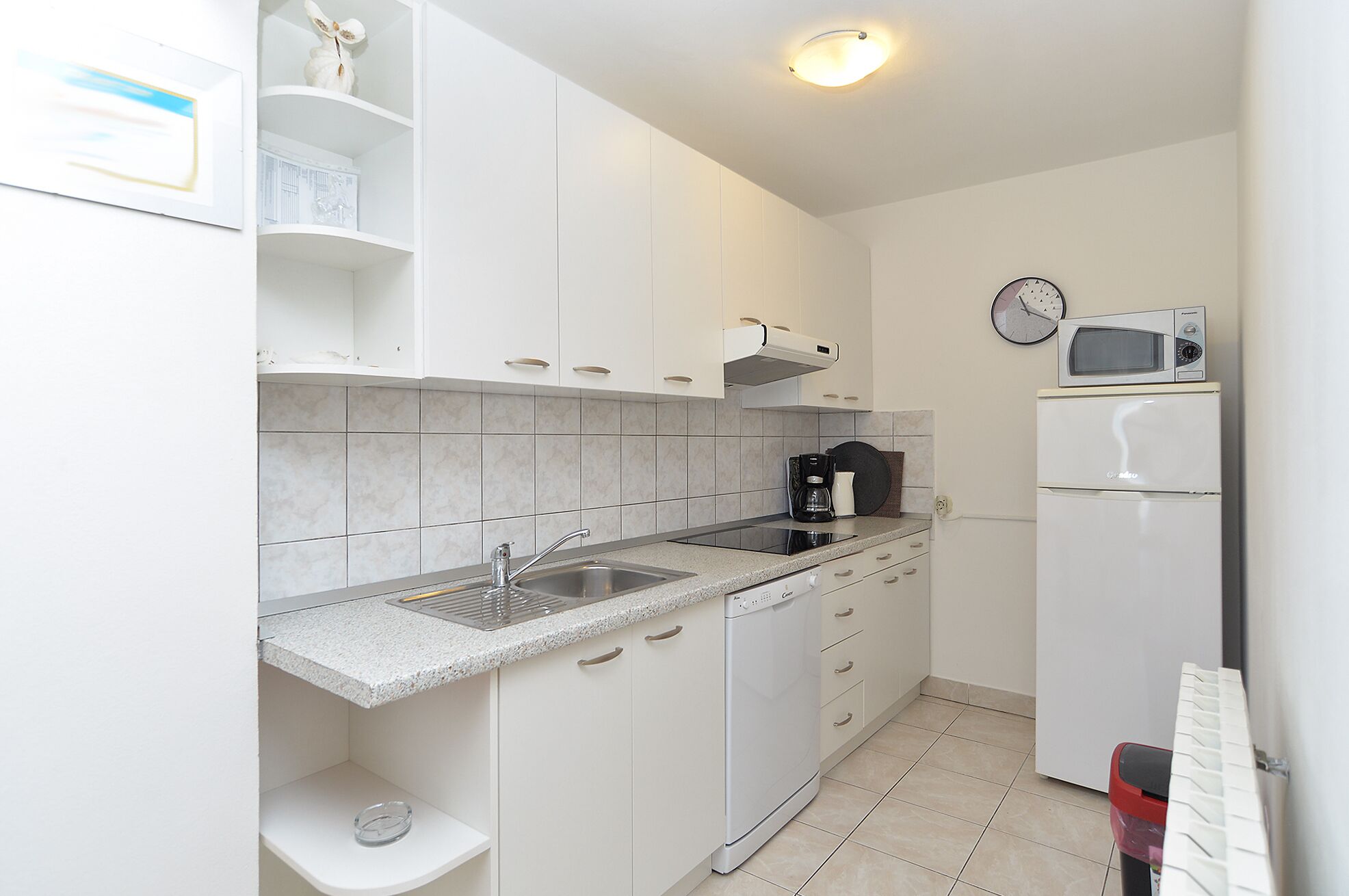 A compact kitchen with white cabinets, a built-in microwave, a coffee maker, and a dishwasher.