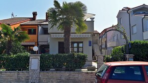 A building with a stone wall, a palm tree, and a red car parked in front. - Apartment 589 (Fazana)
