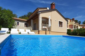 A poolside view of a house with a swimming pool, white lounge chairs, and a stone exterior. - Villa 598 (Tinjan)