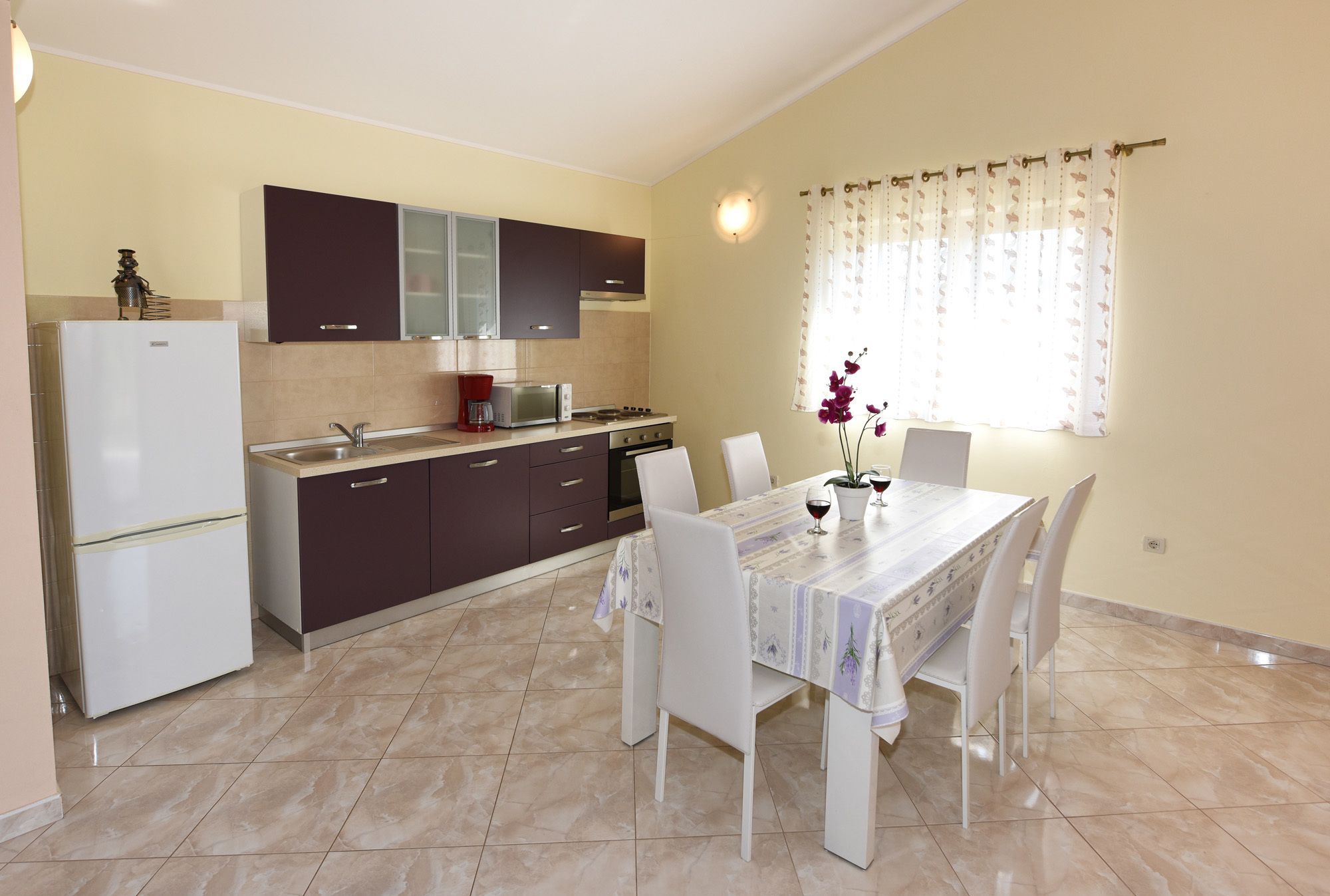 A modern kitchen with a dining area, featuring a refrigerator, stove, cabinets, and a table set for two with chairs.