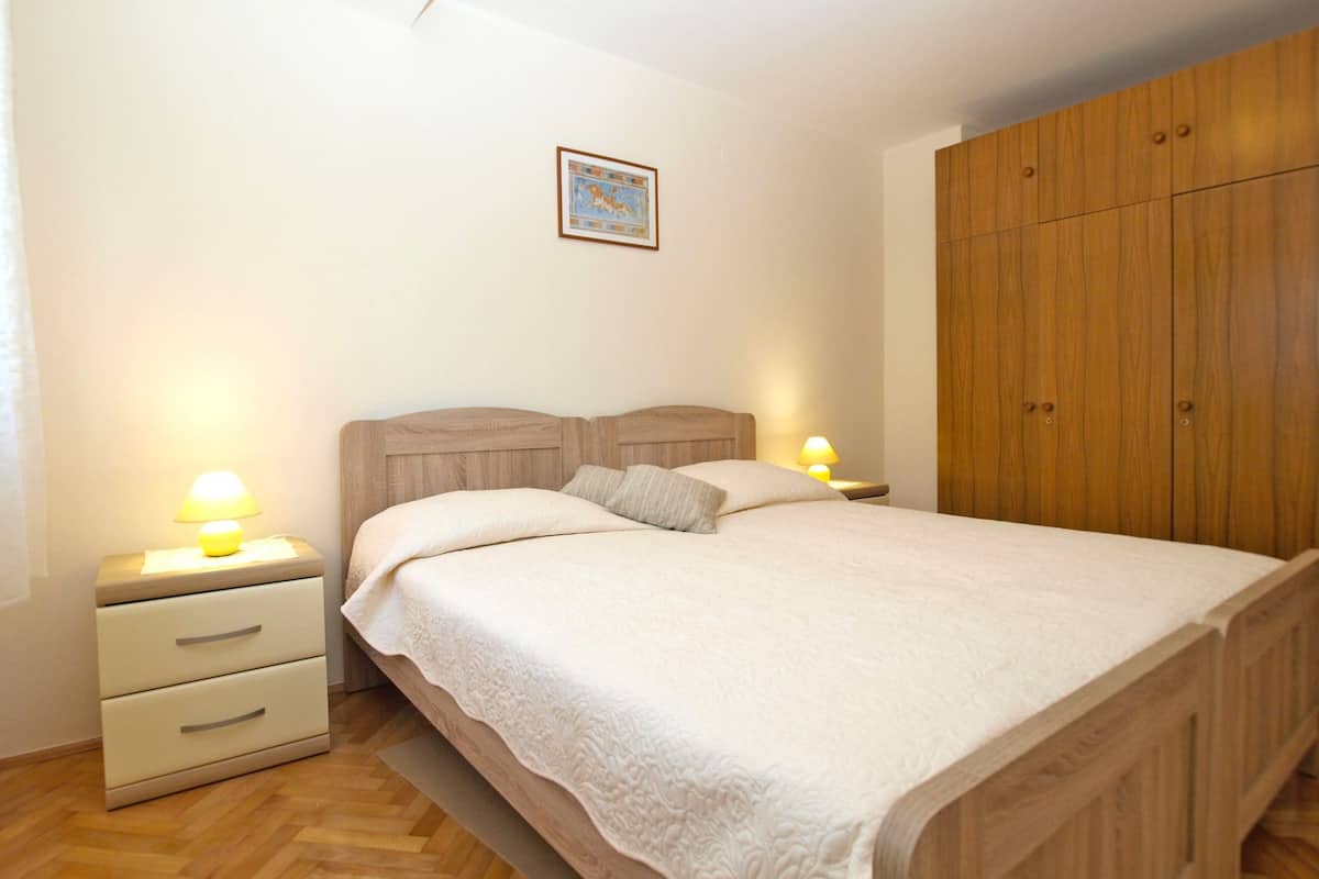 A bedroom with a bed, two bedside tables with lamps, a wooden wardrobe, and a framed picture on the wall.