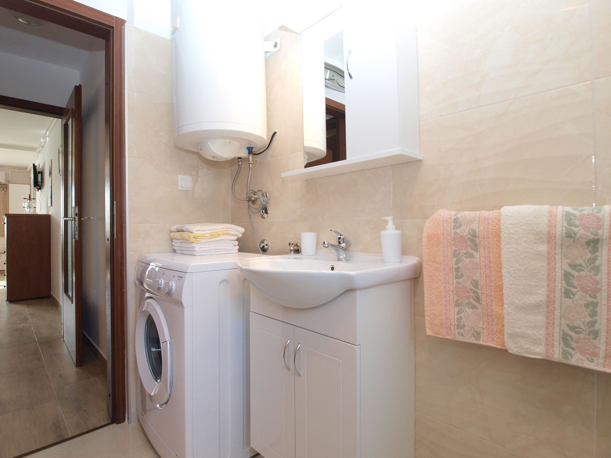 A compact bathroom with a washing machine, a sink, and a mirror.