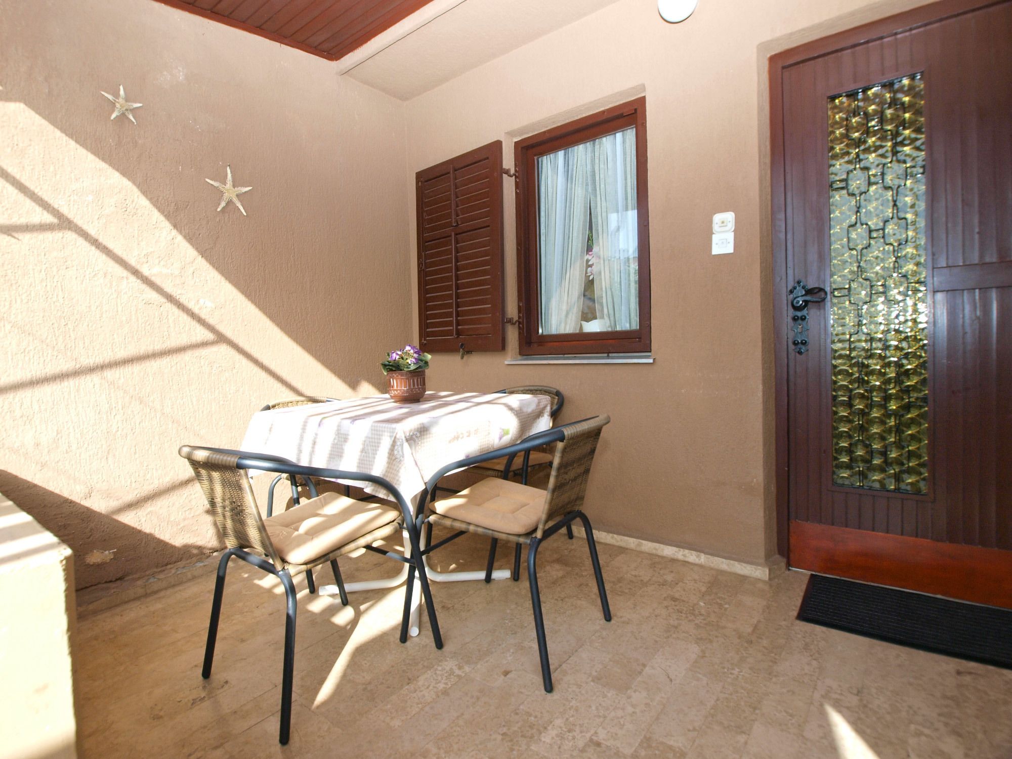 A small patio with a table and chairs, a window with shutters, and a decorative door.