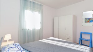 Une chambre à coucher avec un lit, une armoire, une chaise et une fenêtre ornée de rideaux légers.