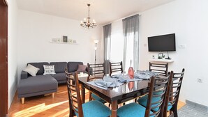 Un coin repas avec une table en bois, des chaises à revêtement bleu, un canapé gris et un lustre.