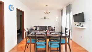 Un coin repas avec une table et des chaises, un lustre, un téléviseur accroché au mur et un canapé à l’arrière-plan.