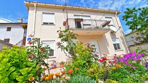 Un bâtiment à deux étages doté d’un balcon, de plantes en pot et d’une variété de fleurs au premier plan.