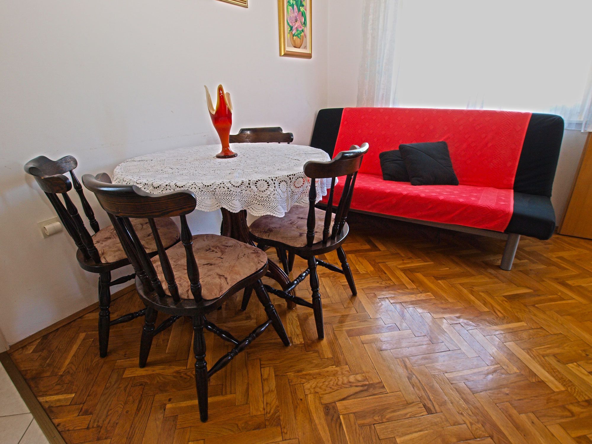 A dining area with a round table, four chairs, and a red sofa.