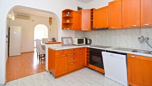 Una cocina compacta con armarios de madera, microondas, lavavajillas y salpicadero de azulejos.