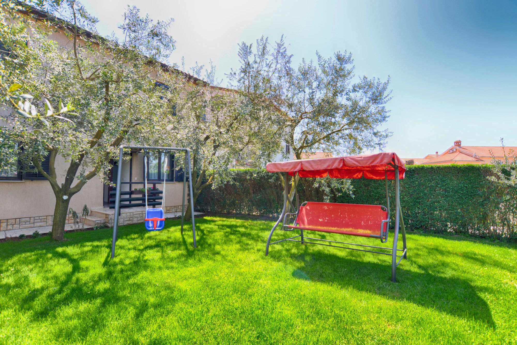 A backyard with a swing set and a red bench under a canopy.