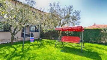 A backyard with a swing set and a red bench under a canopy.