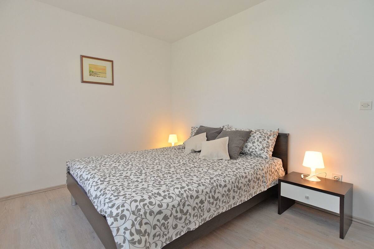 Une chambre à coucher avec un lit, deux tables de chevet, une commode, une lampe et un tableau encadré accroché au mur.