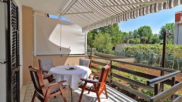 A balcony with a table and chairs, a white awning, and a view of a garden and trees.