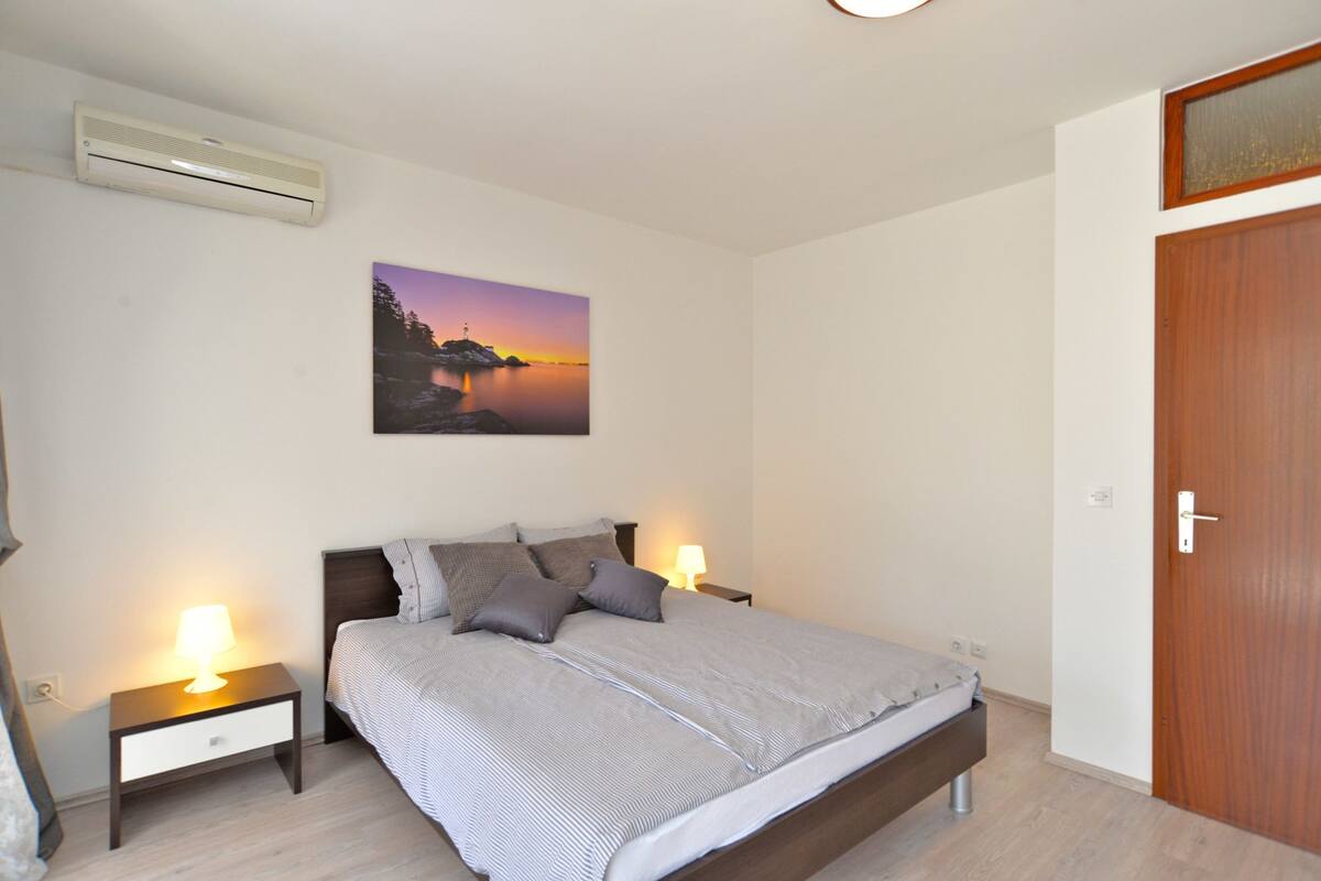 Une chambre à coucher comprenant un lit, deux tables de chevet avec des lampes, un climatiseur fixé au mur et une porte.
