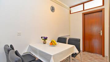 A dining area with a table set for four, a clock on the wall, and a wooden door.
