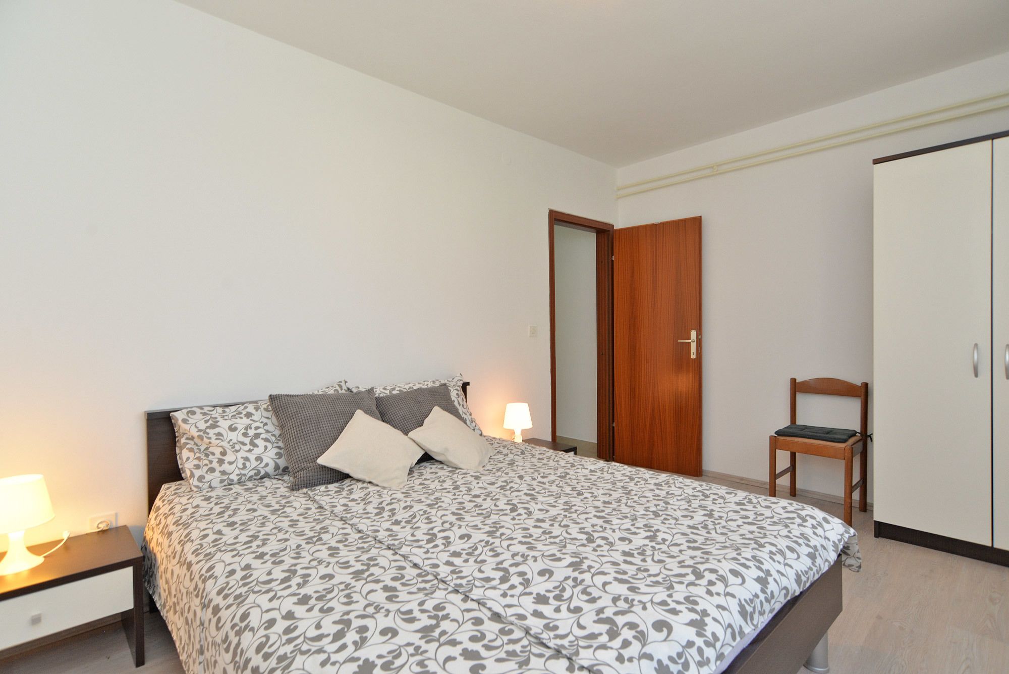 Un dormitorio con cama, lámparas de noche, una puerta de madera y una silla.