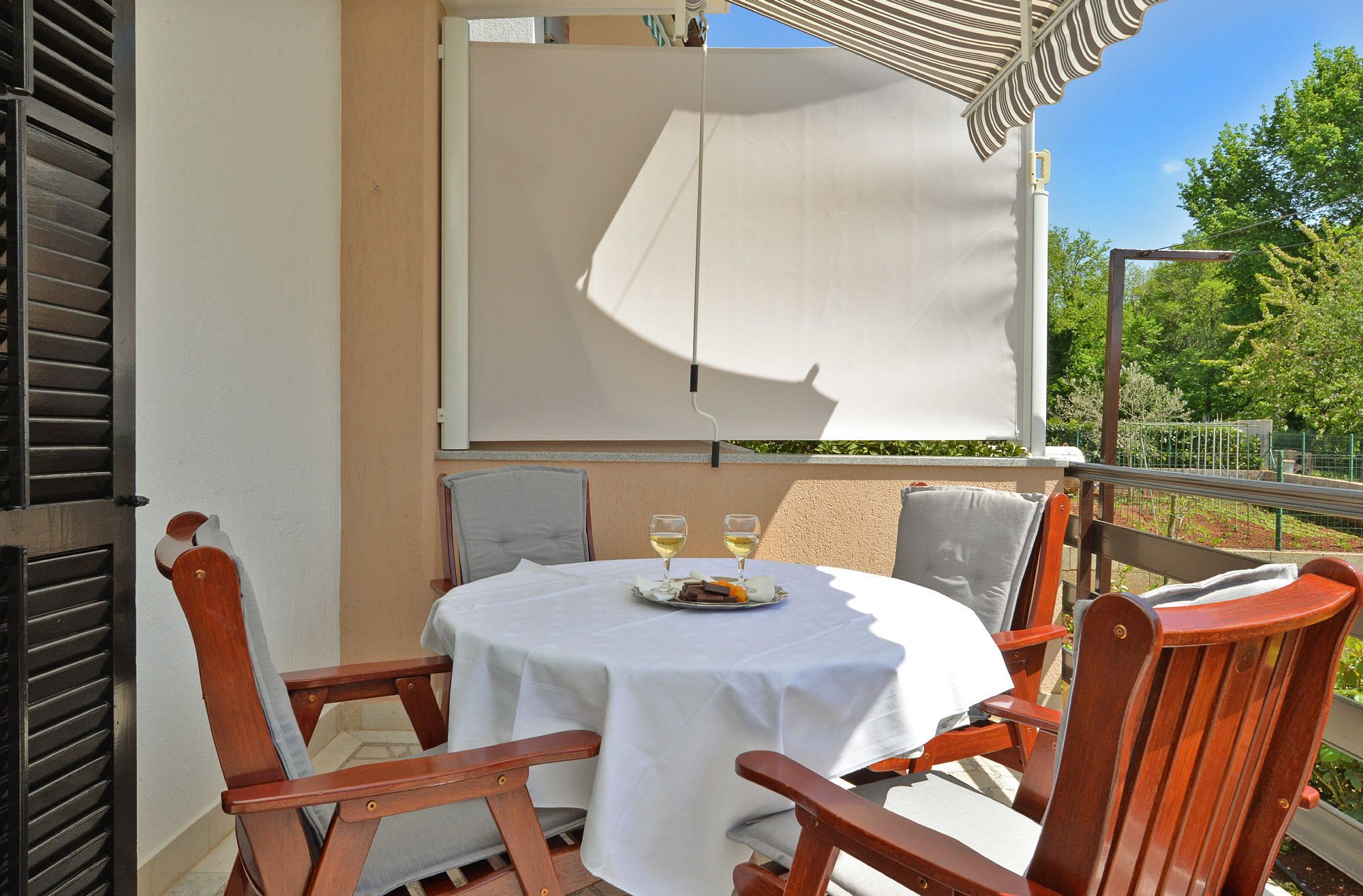 A round table with a white tablecloth, two wooden chairs, and two glasses of white wine on the table.