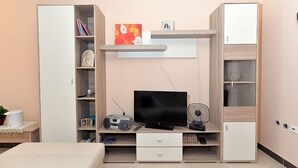A bedroom with a bed, a TV, a radio, and a fan. There are storage cabinets and a shelf with books and a picture frame. - Apartment 640 (Pula)