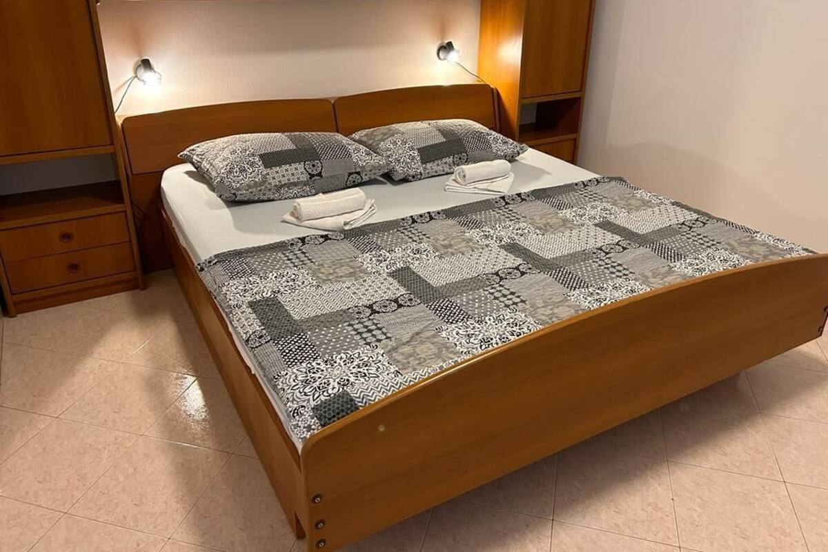 Una cama de madera con colcha y almohadas estampadas, una mesita de noche y una estantería en la pared.