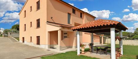Una casa de dos pisos con techo de tejas y un patio cubierto con mobiliario exterior.