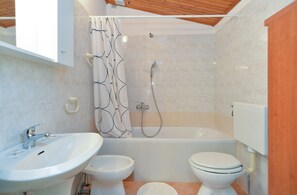 A bathroom with a sink, two toilets, a shower, and a bathtub.