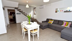 A modern living room with a dining table, grey sofa, and a staircase leading to an upper level. - House 682 (Svetvincenat)