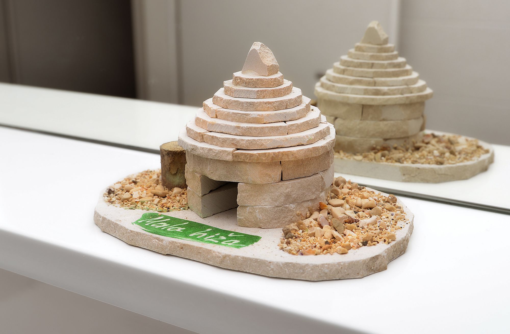 Une maquette d’une maison en pierre avec une enseigne verte sur la façade.