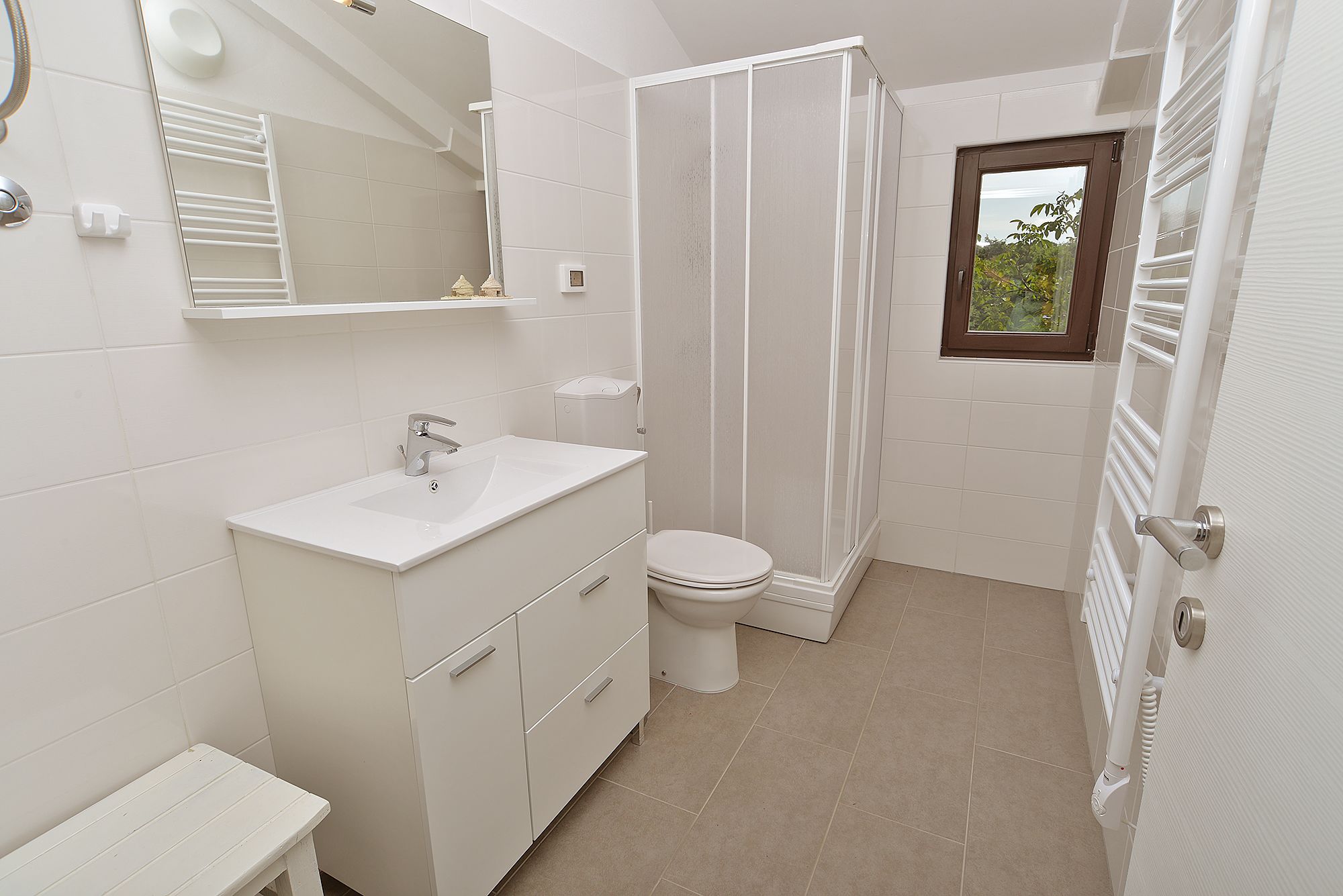 Baño con lavamanos, inodoro y cabina de ducha blancos.
