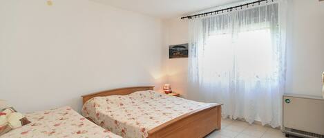 A bedroom with two wooden beds, a nightstand, a radiator, and a window with sheer curtains.