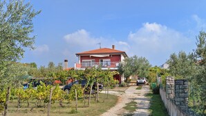 Ein rotes Haus mit Balkon, umgeben von Weinbergen und parkenden Autos.