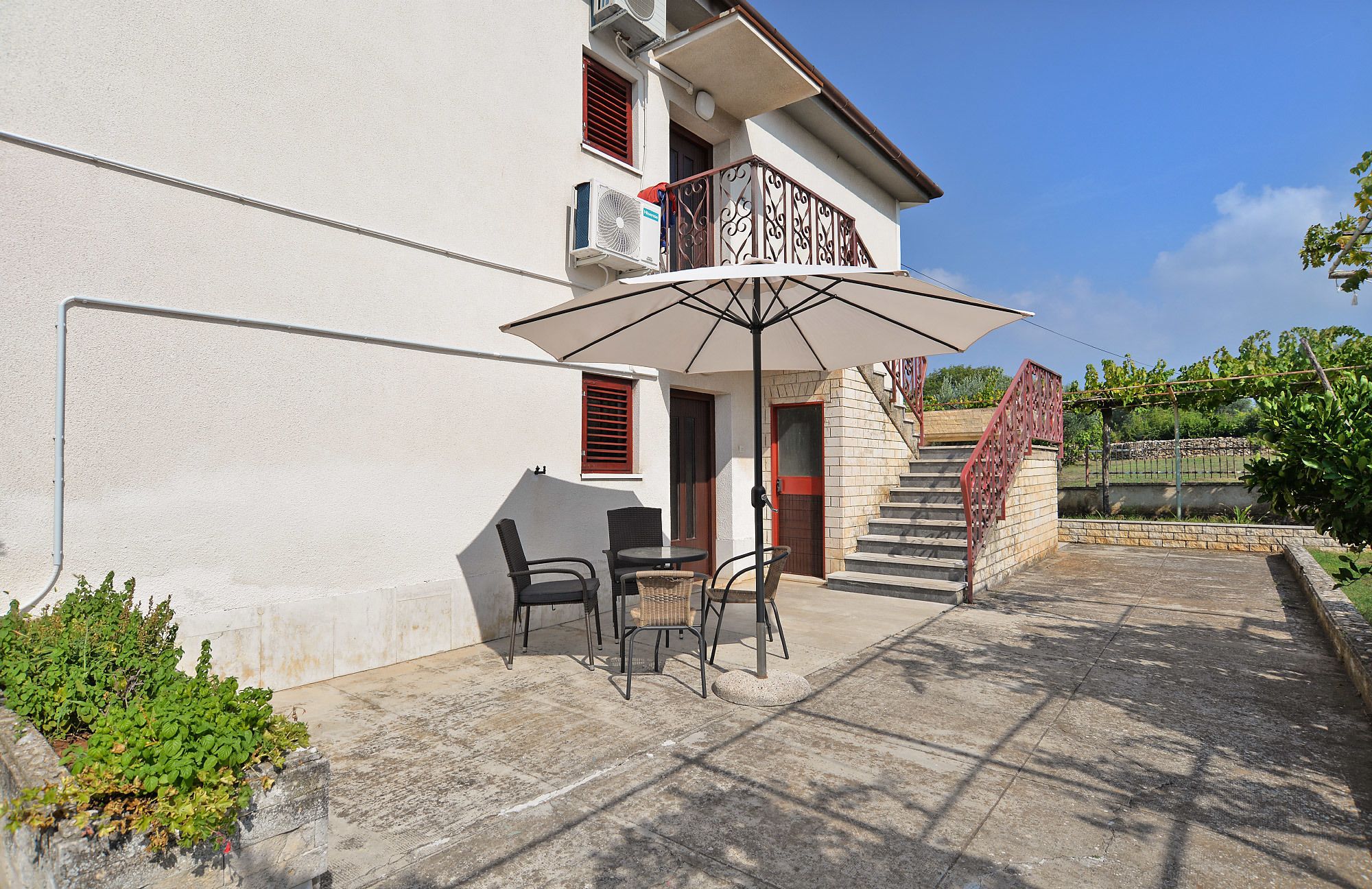 A two-story building with a balcony, outdoor seating area with chairs and a table, and a staircase leading to the upper floor.