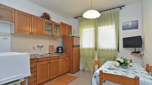 Eine kleine Küche mit Holzschränken, einem Kühlschrank, einer Kaffeemaschine und einem Esstisch mit Tischdecke.