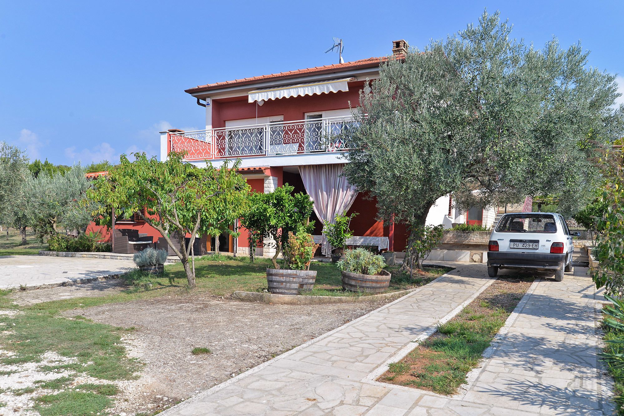 A two-story building with a balcony, surrounded by trees and a parked car.