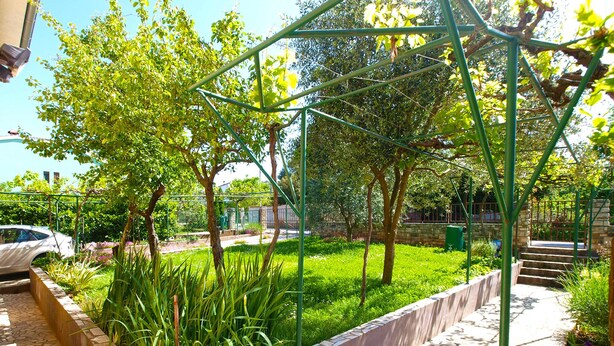 A garden with a pergola, stone pathway, and a car parked nearby. - Apartment 686 (Pula)