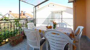A covered outdoor dining area with a table and chairs, a potted plant, and a view of a building in the background. - Apartment 686 (Pula)