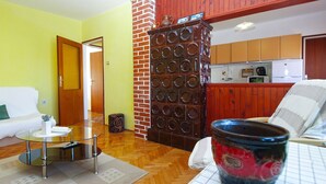 A living room with a glass coffee table, a sofa, a decorative brick wall, and a kitchen area in the background. - Apartment 686 (Pula)