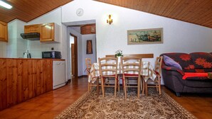 Uma sala de estar acolhedora com uma mesa de jantar, cadeiras, sofá e uma cozinha com armários de madeira e eletrodomésticos.