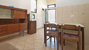 A kitchen with a wooden cabinet, a dining table with chairs, and a television on a small cabinet. - Apartment 695 (Pula)
