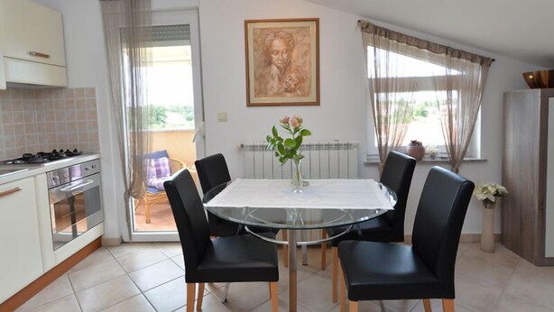 A modern kitchen with a gas stove, oven, and a dining area with a glass table and black chairs. - Apartment 696 (Fazana)