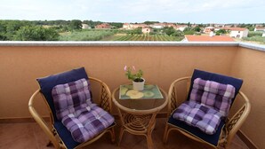 A balcony with two wicker chairs and a small table, a potted plant, and a view of a residential area. - Apartment 696 (Fazana)