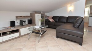 A modern living room with a dark leather sofa, a glass coffee table, a white cabinet, and a built-in TV. - Apartment 696 (Fazana)