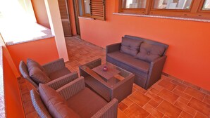 Zona de pati amb mobles de vimet, incloent un sofà i dues butaques, una taula de vidre per a cafè i una taula petita amb una espelma.