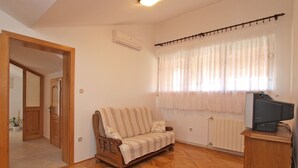 Habitació amb sòl de fusta en relllaç, un sofà de fusta, una televisió sobre un suport de fusta i un radiador.