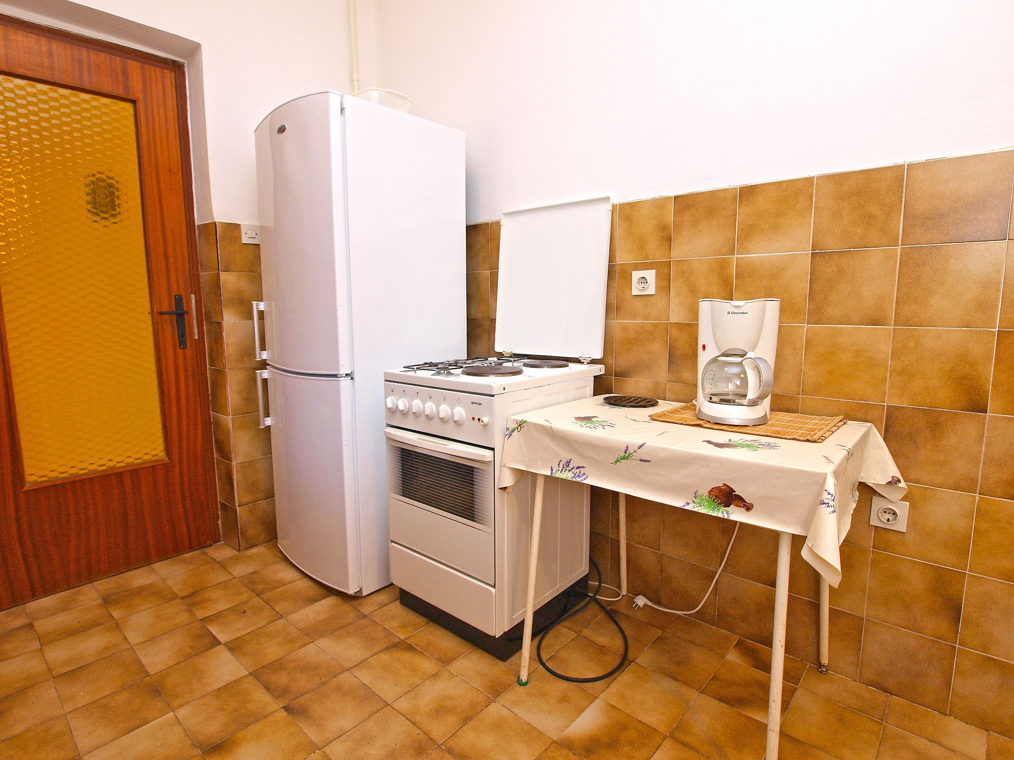 A compact kitchen with a refrigerator, stove, and coffee maker.