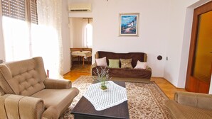 A living room with a brown sofa, two armchairs, a coffee table with a lace table runner, and a painting on the wall. - Apartment 711 (Fazana)