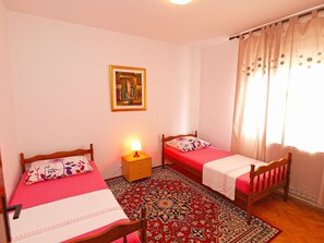 A room with two wooden beds, a red and white patterned rug, a small wooden nightstand with a lamp, and a painting on the wall. - Apartment 711 (Fazana)