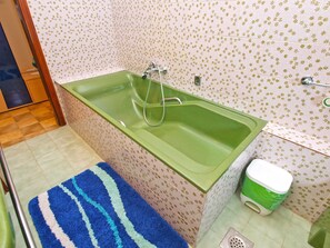 A bathroom with a green bathtub, a shower, a toilet, and a blue and white striped rug. - Apartment 711 (Fazana)