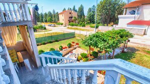 A residential area with a staircase leading to a balcony, a garden with various plants, and a building with a red roof in the background. - Apartment 711 (Fazana)