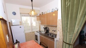 A compact kitchen with a table, a refrigerator, a stove, and a sink. - Apartment 712 (Medulin)